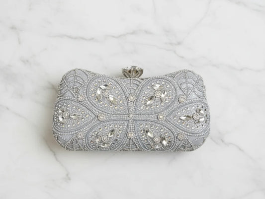 Silver clutch bag with intricate gemstone design on a white marble background